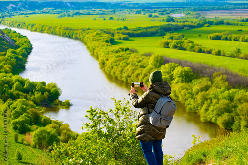 a tourist girl takes pictures on her smartphone of a beautiful mountain landscape against the background of a river and a green field. selective focus