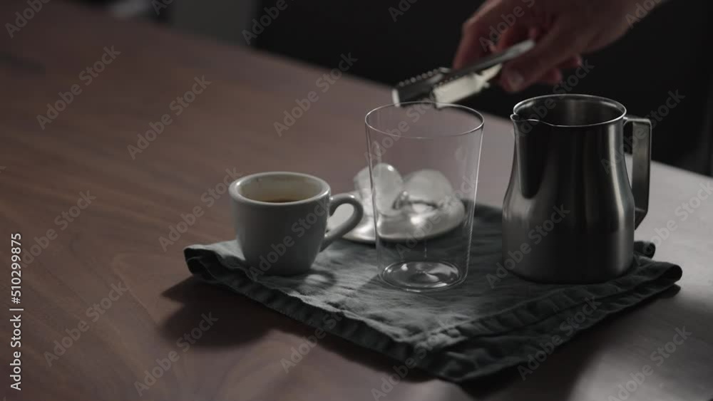 Slow motion man making espresso tonic in tumbler glass on walnut table