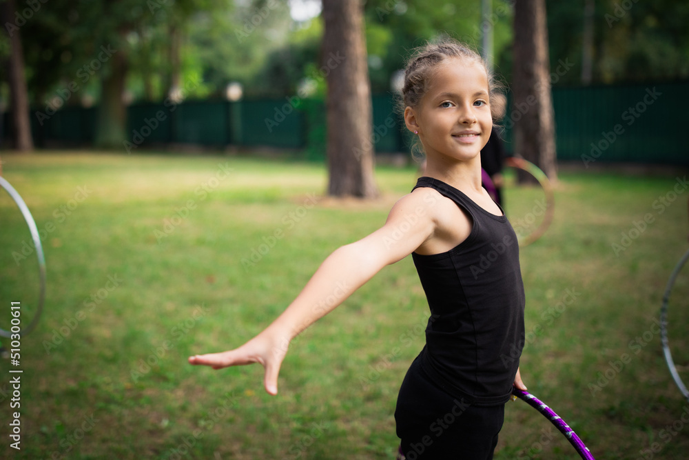 Girl doing exercise with hoop on rhythmic gymnastics training with other trainees outdoors in sports camp in summer Girl doing exercise with hoop on rhythmic gymnastics training with other trainees outdoors in sports camp in summer