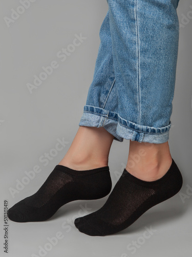 A cropped side view of a beautiful woman's legs in black socks, isolated against a gray background. Young woman walking on tiptoes. Comfortable footwear for ladies and girls. Cozy women's hosiery.