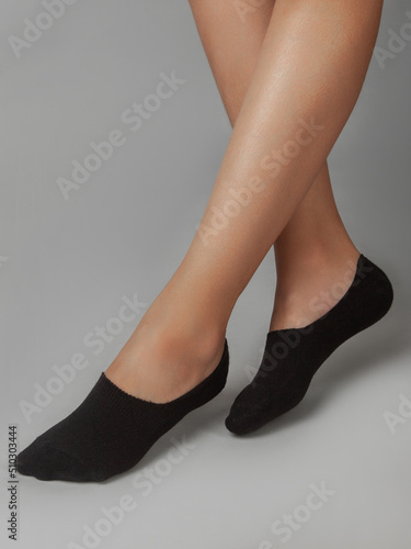 A cropped side view of a beautiful woman's legs in black socks, isolated against a gray background. Young woman walking on tiptoes. Comfortable footwear for ladies and girls. Cozy women's hosiery.
