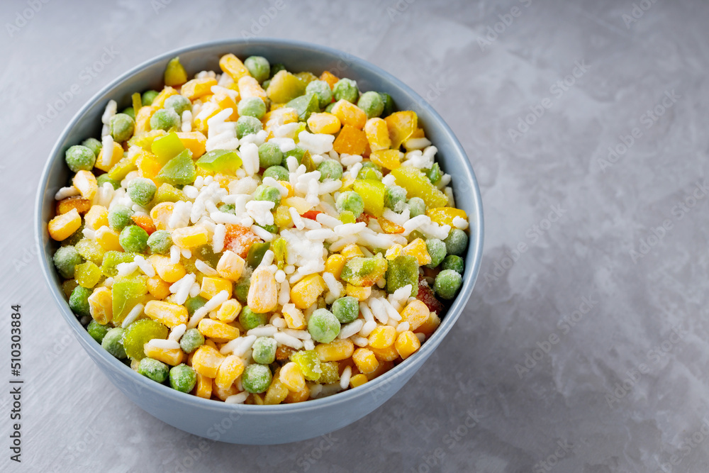 Bowl with mixed frozen vegetables with rice on a gray background. Frozen vegetables retaining all nutrients: green peas, corn, bell pepper. Healthy food concept. Top view. Copy space Bowl with mixed frozen vegetables with rice on a gray background. Frozen vegetables retaining all nutrients: green peas, corn, bell pepper. Healthy food concept. Top view. Copy space