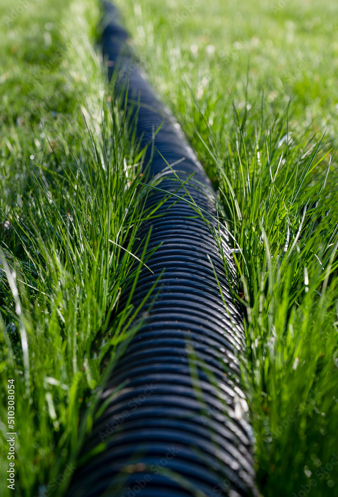 Foto de Black corrugated plastic pipe on green grass. Pipes for use in