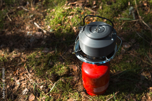 Cooking, heating a tourist kettle on a portable gas burner with a red gas cylinder. Camping, a man cooks breakfast outdoors. Summer outdoor activities