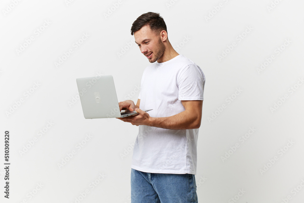 Happy passionate enjoyed tanned handsome man in basic t-shirt chatting with friends by laptop posing isolated on over white studio background. Copy space Banner Mockup. Gadgets lifestyle concept Happy passionate enjoyed tanned handsome man in basic t-shirt chatting with friends by laptop posing isolated on over white studio background. Copy space Banner Mockup. Gadgets lifestyle concept