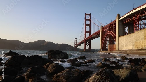 Golden Gate Bridge near sunset with ocean waves crashing into rocks