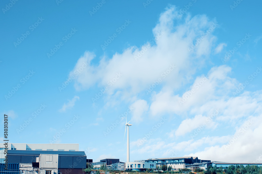 Wind turbine in the middle of industrial estate as a source of renewable energy on blue sky background