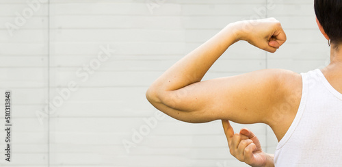 Woman Back Portrait. A faceless  woman shows the flabby muscles of the arm with her index finger. Flabby Arm Syndrome (FAS). Effect of aging caused by loss of elasticity and muscle. Banner, copyspace.