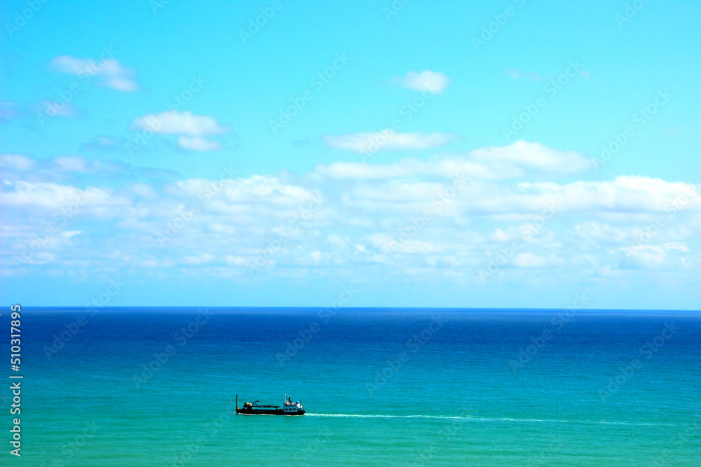 Heavenly view of the Adriatic Sea in Ortona with intensifying blue color reaching up to the horizon and a white-black boat lightly skimming its surface