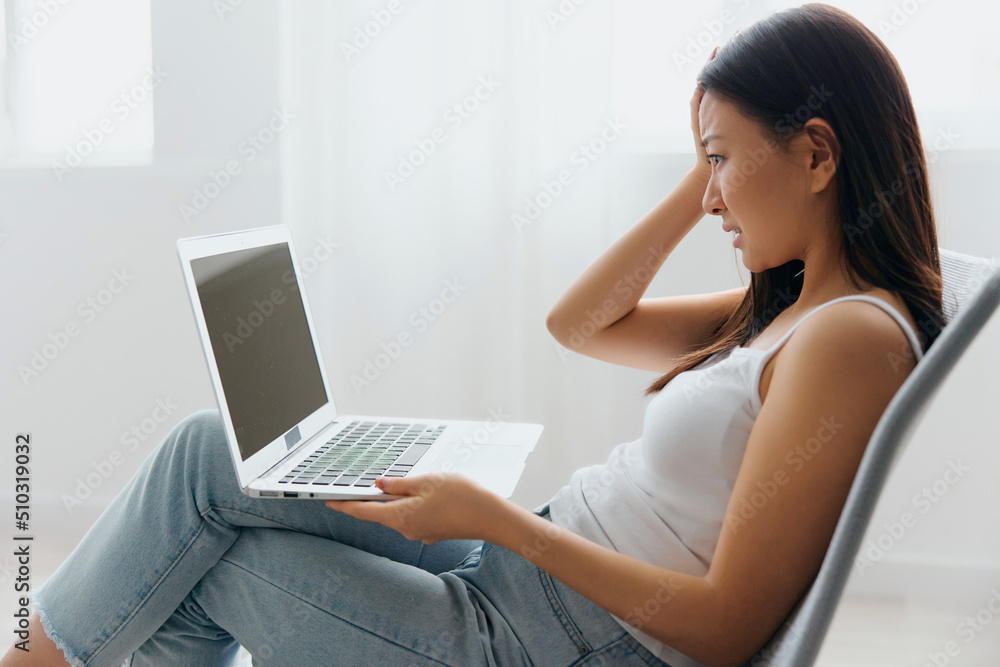 Upset unhappy confused tanned lovely young Asian woman shocked by gadget breakdown at home interior living room. Distance communication, Remote work, Social media concept. Cool offer Banner Mockup Upset unhappy confused tanned lovely young Asian woman shocked by gadget breakdown at home interior living room. Distance communication, Remote work, Social media concept. Cool offer Banner Mockup