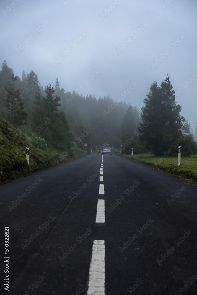 Road trip with a car driving though the road with fog and mist. Exploring the Azorean nature. Sete Cidades, Island of São Miguel in the Azores, Portugal. Road trip with a car driving though the road with fog and mist. Exploring the Azorean nature. Sete Cidades, Island of São Miguel in the Azores, Portugal.