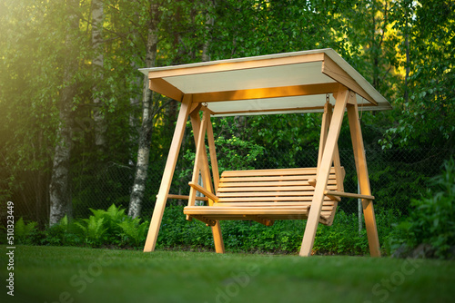 Wooden swing in the green garden. Recreation in the park. Garden design. Relax in the fresh air. Garden furniture made of wood. photo