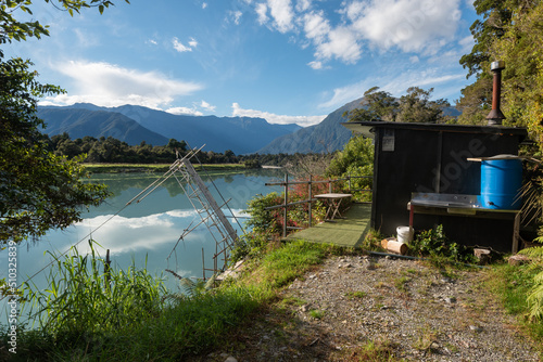 Φωτογραφία A whitebaiter's hut and raised fishing platform, or stand, by the flat calm waters of the lower Waiatoto River