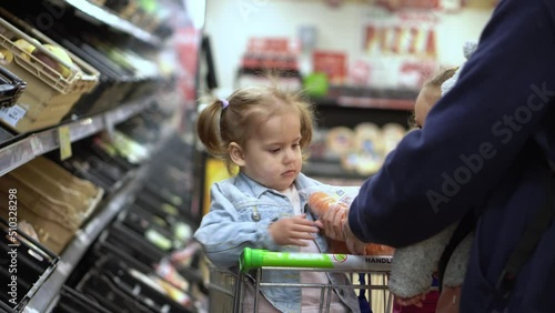 Shopping list food crises concepts. Father with Two daughters at Supermarket. Children sitting in cart. Kids Siblings with Dad buy fresh vegetables and fruits. Healthy eating Lifestyle. Fatherhood
