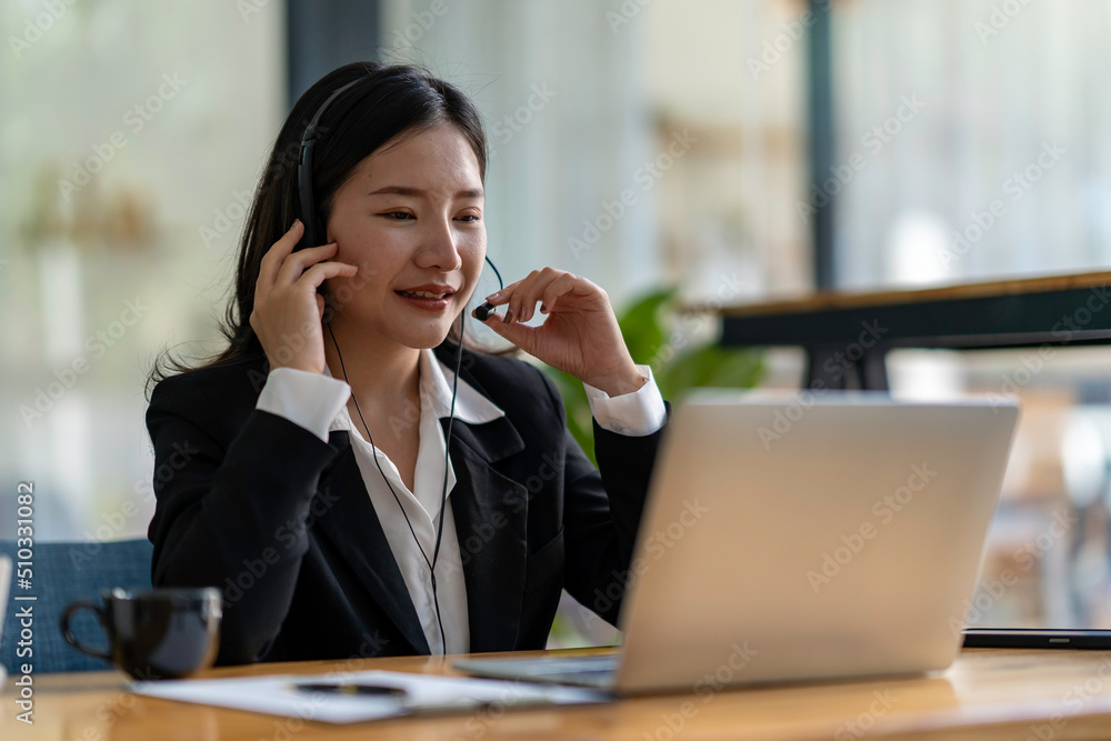 Happy Asian woman sitting in the office and video conference with a business partner on a laptop. Concept of a new lifestyle and social distancing Happy Asian woman sitting in the office and video conference with a business partner on a laptop. Concept of a new lifestyle and social distancing