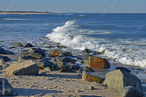 Light ocean breezes cause rolling waves into the rocky shore at a Sandy Hook, New Jersey, beach, with the NYC skyline in the hazy background -08 photo