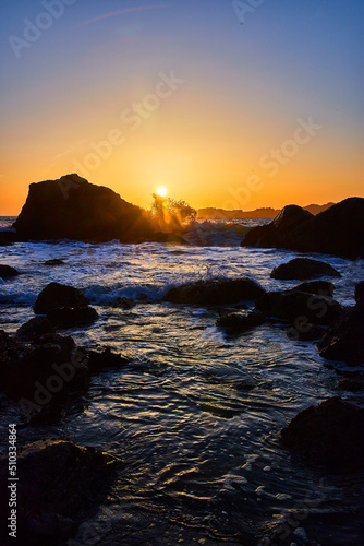 Sun sets on beach with waves and rocks