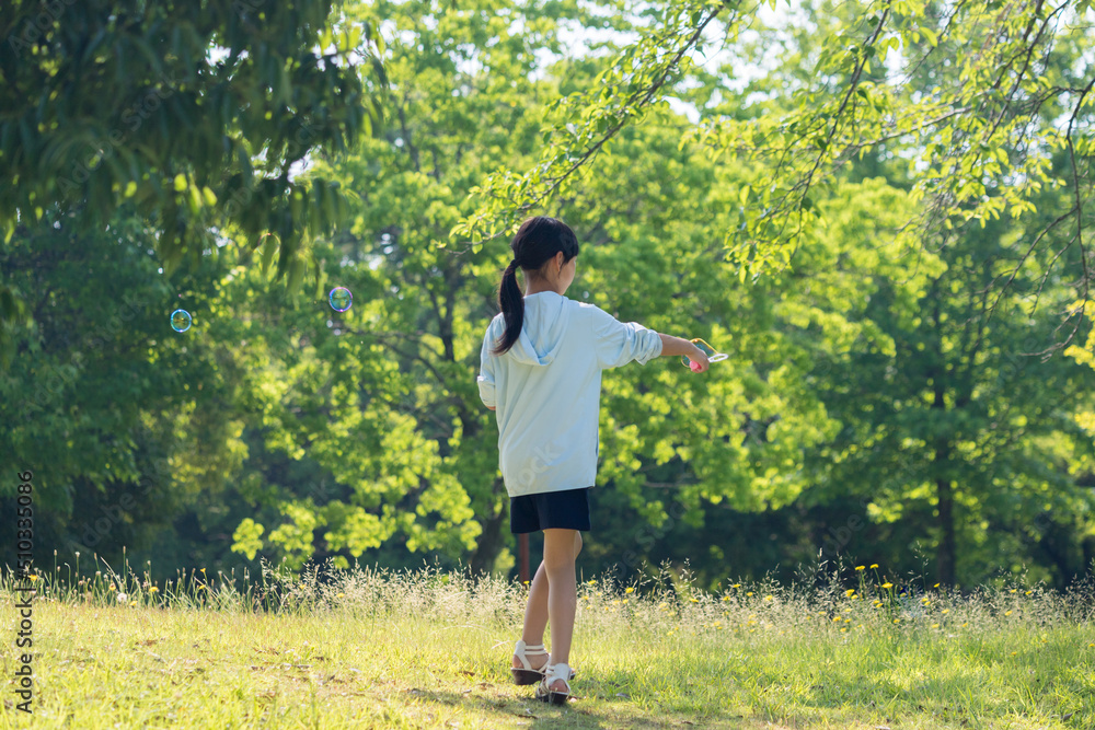夏の公園でシャボン玉を遊んでいる小学生の女の子の様子 夏の公園でシャボン玉を遊んでいる小学生の女の子の様子