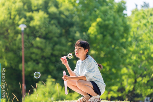 夏の公園でシャボン玉を遊んでいる小学生の女の子の様子