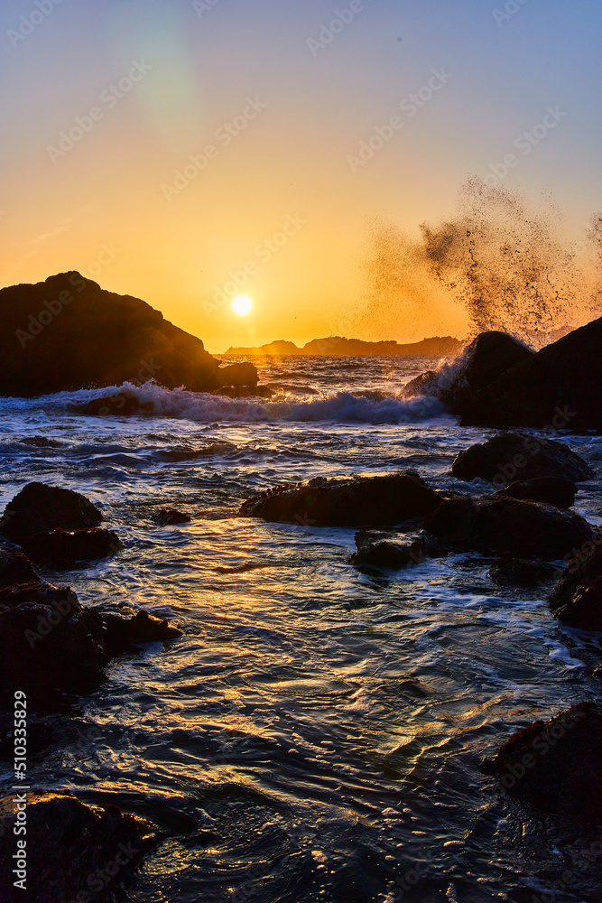 Sunset on west coast beach with waves crashing over rocks
