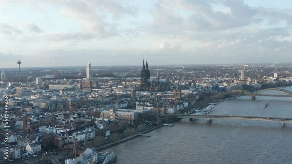Backwards fly above Rhine river in city at dusk. Busy bridges over rippled water surface. Gothic Kolner Dom towering above surrounding development. Cologne, Germany Backwards fly above Rhine river in city at dusk. Busy bridges over rippled water surface. Gothic Kolner Dom towering above surrounding development. Cologne, Germany