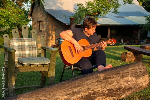Senior woman sitting in nature and playing guitar