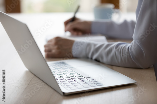 Unknown woman working studying sit at desk with laptop  holds pen write up information  makes list to-do use personal paper organizer  jotting notes  close up. Prepare report  doing paperwork concept