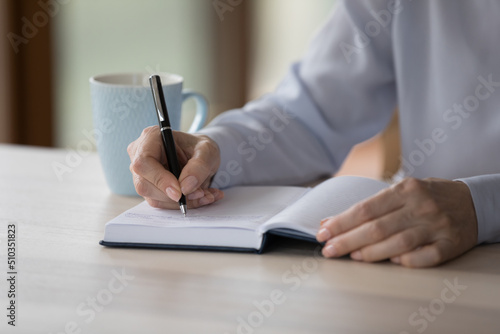 Close up middle-aged woman sit at desk write in paper planner, create important notes or meetings not to forget, jotting business plans and tasks memos. Week goals, to-do list, time management concept