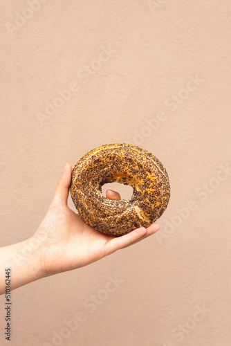 bagel with poppy seeds in hand on a beige background