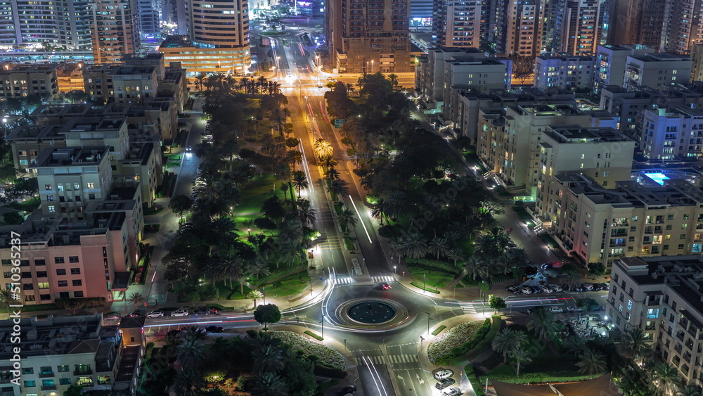 Traffic on a road with roundabout and low rise buildings in Greens district aerial night timelapse. Traffic on a road with roundabout and low rise buildings in Greens district aerial night timelapse.
