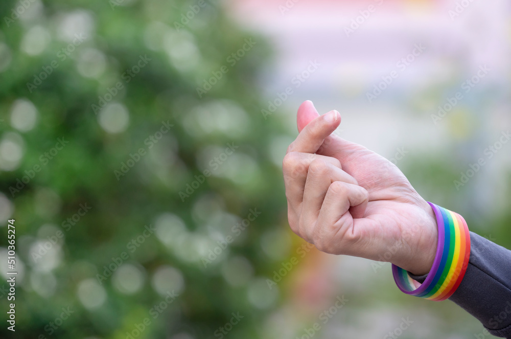 man wearing lgbt rainbow wristband doing mini heart hand sign for love, encourage to LGBTQ community equality movement, LGBTQ happy pride month concept. man wearing lgbt rainbow wristband doing mini heart hand sign for love, encourage to LGBTQ community equality movement, LGBTQ happy pride month concept.