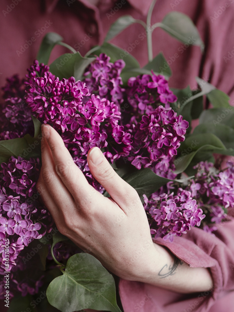 The girl holds a bouquet of lilacs on the background of a pink shirt. Spring concept The girl holds a bouquet of lilacs on the background of a pink shirt. Spring concept