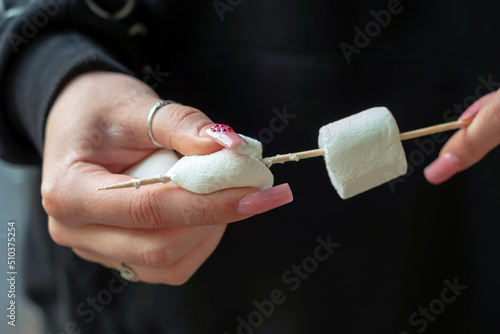 a person's hands are impaled on a wooden skewer - a sweet marshmallow delicacy popular in the USA for barbecue.