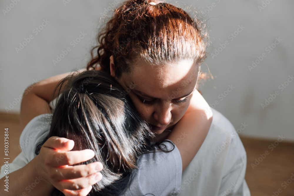 Naklejka premium Portrait of abused family. Young sad woman holding girl, protecting, consoling. Scared daughter hugging mother. Domestic violence, family conflicts, abuse, fighting, aggression, quarreling, care. 