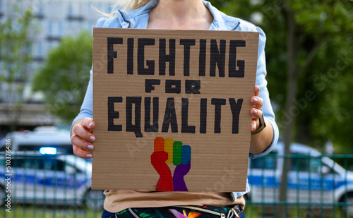 Woman holding placard sign Fighting for Equality with rainbow flag fist, during LGBT Pride Parade. People at equality march to support and celebrate LGBT+, LGBTQ gay and lesbian community.