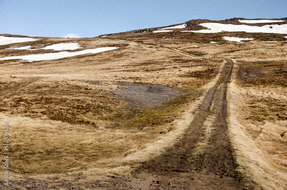 Dirt road leading up to a pass in an area with low, partly snow-covered mountains near Hvammstangi in Iceland