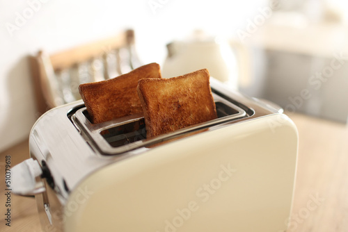 Toasted bread and toaster for breakfast. Modern white toaster and roasted bread slices toasts inside on wooden table in kitchen.