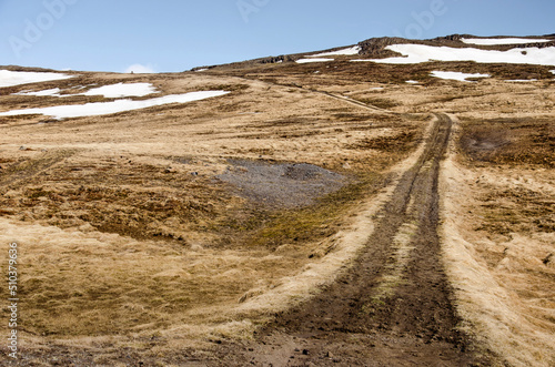 Dirt road leading up to a pass in an area with low  partly snow-covered mountains near Hvammstangi in Iceland