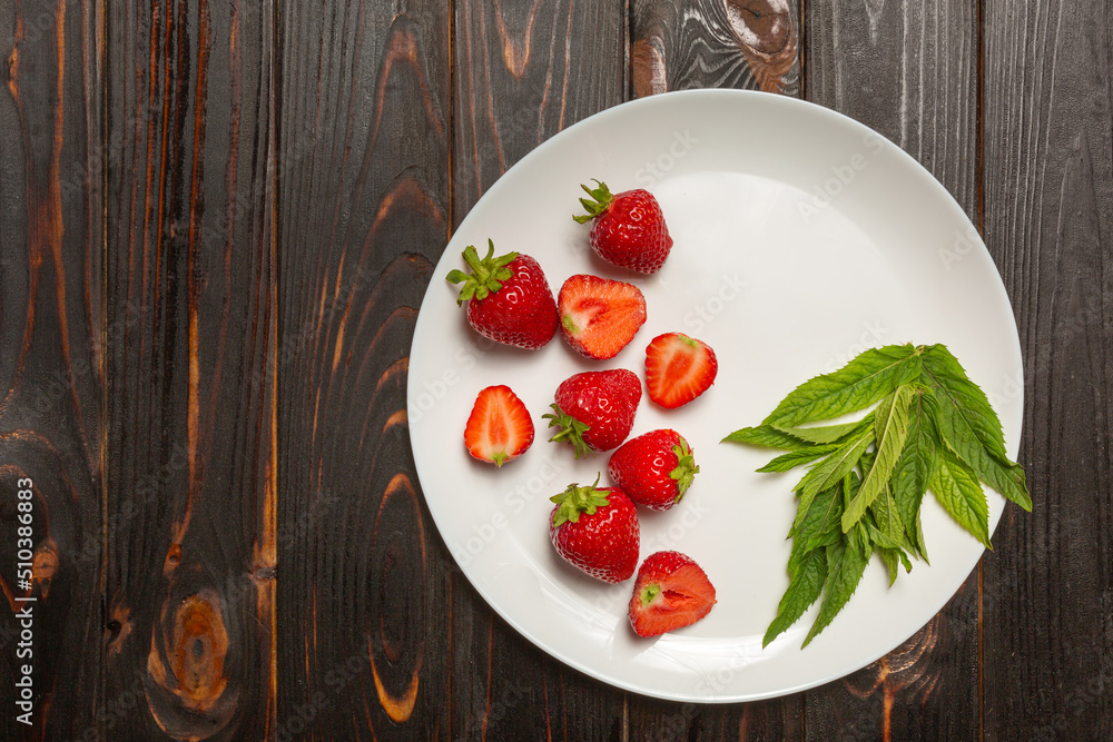 on a dark wooden table a white plate with freshly picked strawberries. Copy space on a dark wooden table a white plate with freshly picked strawberries. Copy space