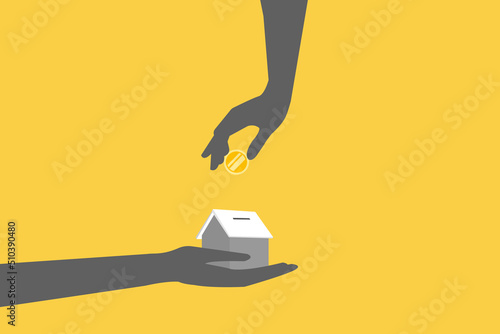 Close up of hand putting coin in house piggy bank.