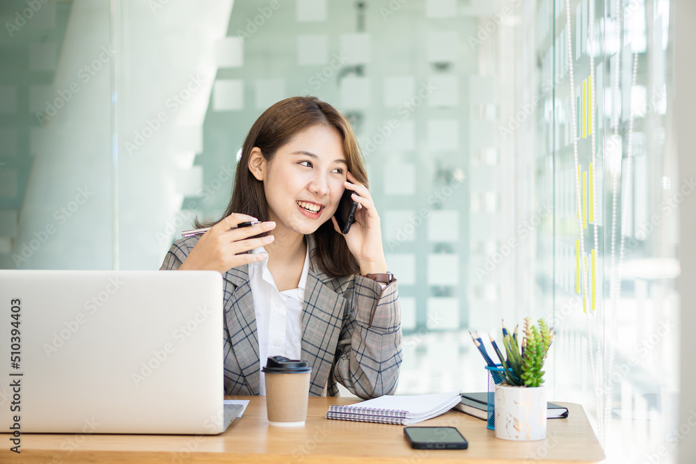 Portrait of Asian businesswoman talking on smartphone writing on laptop computer in home office Startup business sme telemarketing beautiful woman working in modern office Portrait of Asian businesswoman talking on smartphone writing on laptop computer in home office Startup business sme telemarketing beautiful woman working in modern office