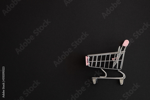 Mini pink shopping cart on black background. Shopping concept