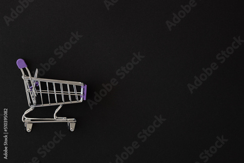 Mini violet shopping cart on black background. Shopping concept