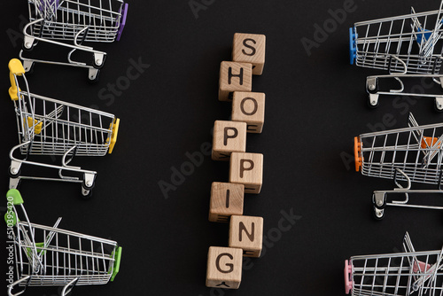 Mini color supermarket trolleys and word shopping on black background. Shopping concept