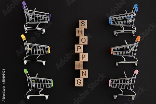 Mini color supermarket trolleys and word shopping on black background. Shopping concept