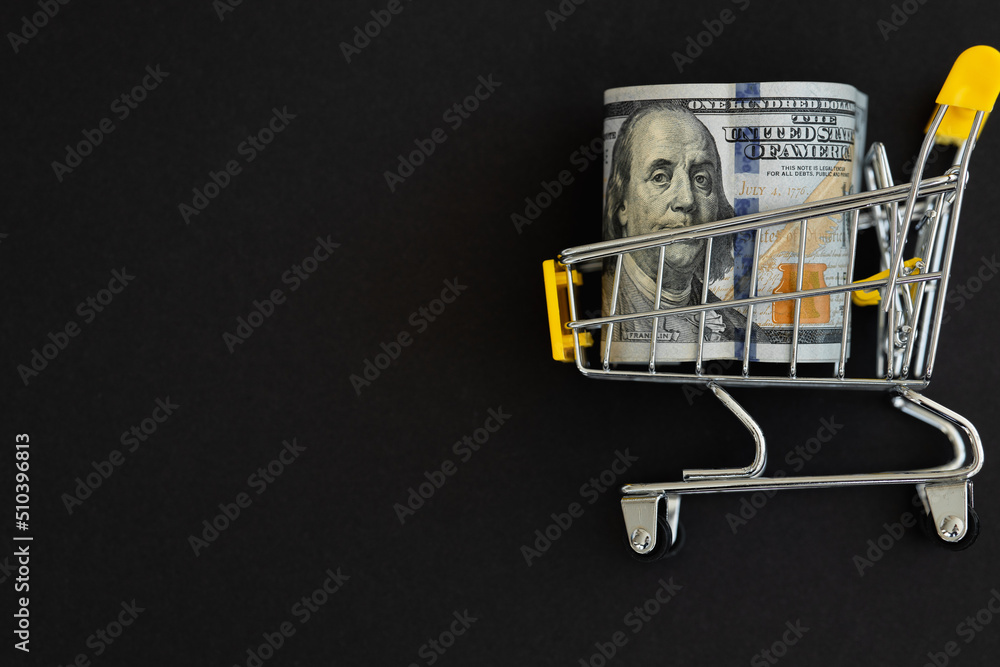 Small shopping cart with 100 dollar banknote on black background