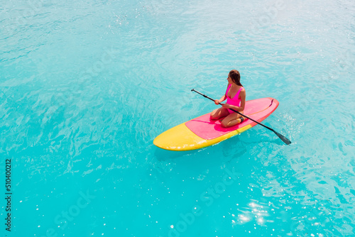 Attractive woman in pink swimwear floating on stand up paddle board on a quiet ocean. SUP surfing with woman in tropical sea © artifirsov