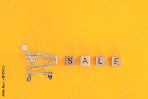 Small metal cart and word sale on yellow background. Shopping concept