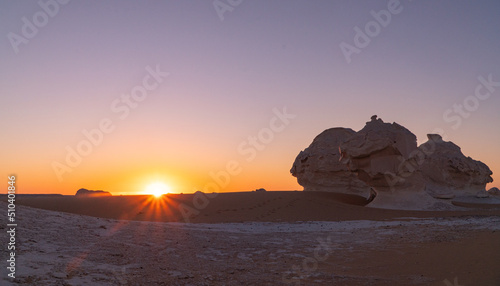 sunrise in the white desert with the sun coming up behind the rock formations in Egypt