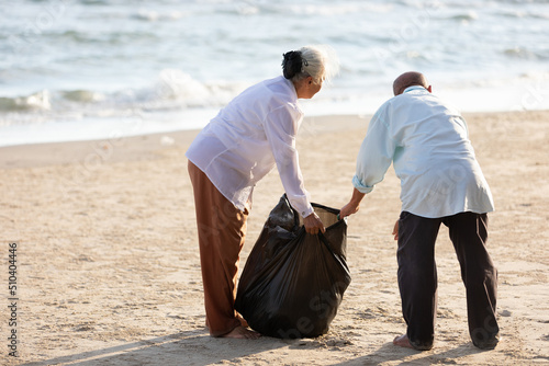 senior people volunteer keeping and picking trash into garbage bag on the beach